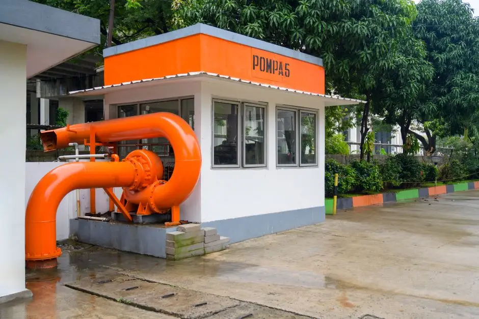 Bright orange pump station structure in Jakarta with greenery around.